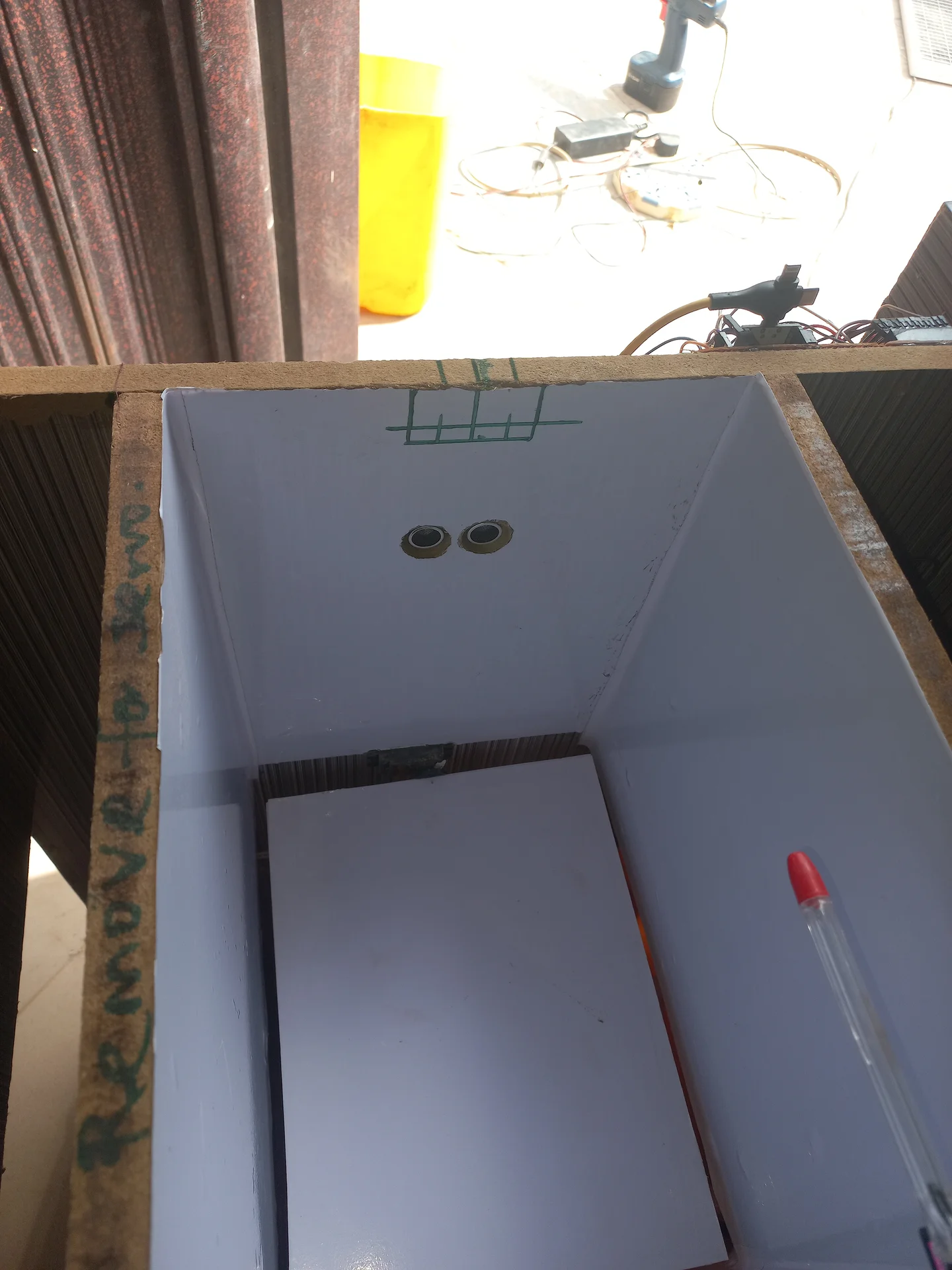 Angled top-down view into the bin showing two ultrasonic sensors on the interior front wall, with the white-lined sorting tray and a marker pen visible below