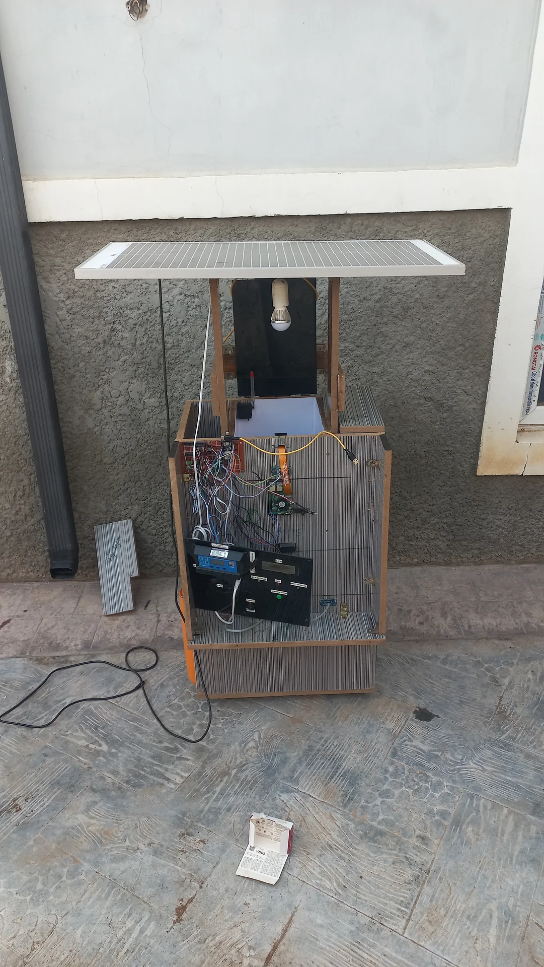 Full system view showing the bin, the overhead wooden frame, and the solar panel mounted flat on top, with the battery visible in the open electronics bay
