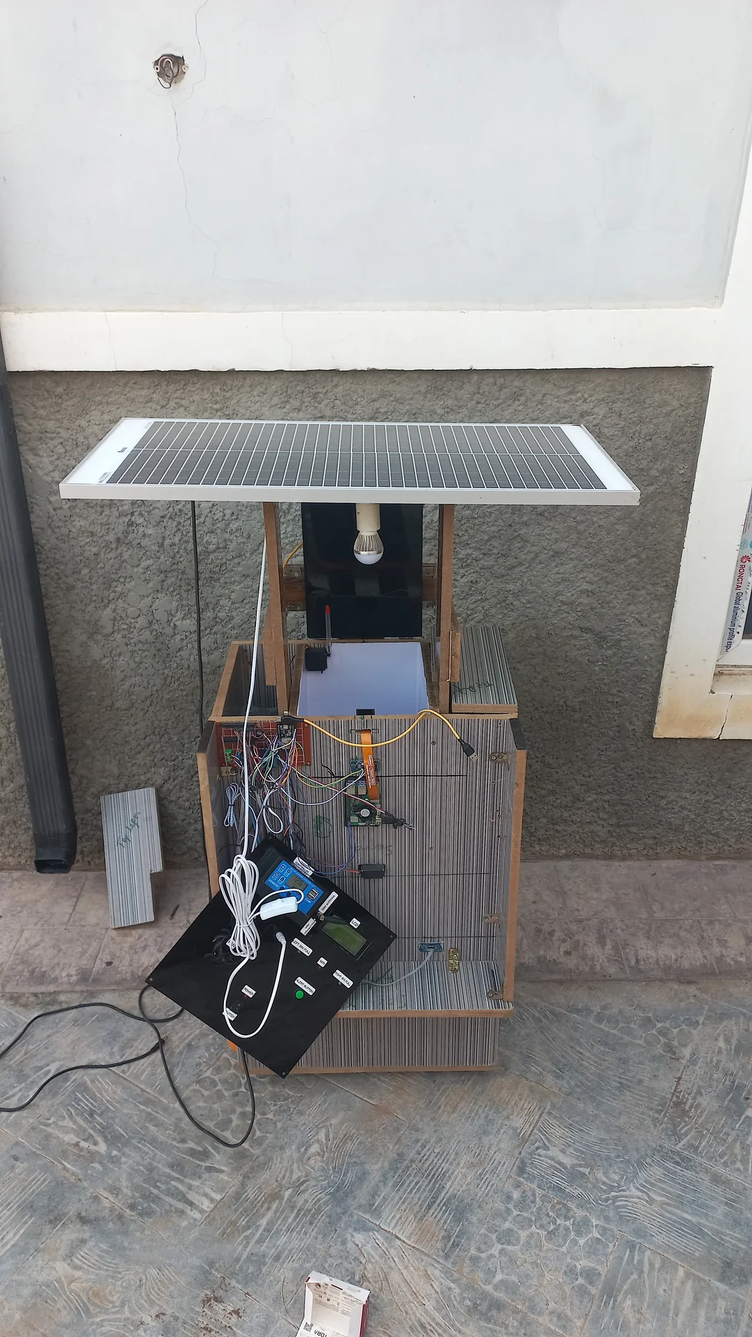 The integrated system with the solar panel mounted horizontally on the wooden overhead frame above the bin, showing the full physical assembly together