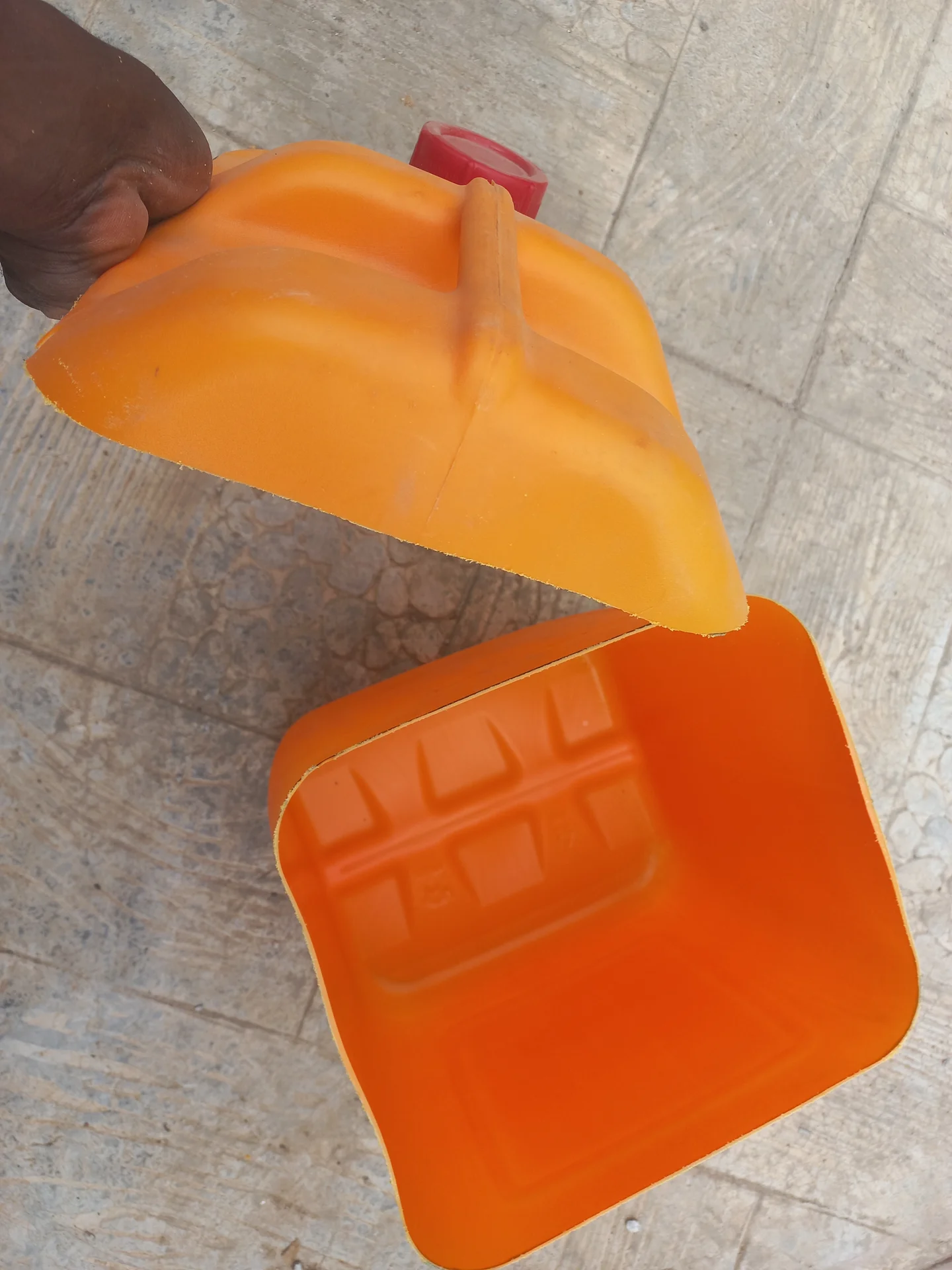 Orange jerry can cut near the base, with the top section held up and the shallow bottom tray section visible below, showing the open interior of both pieces