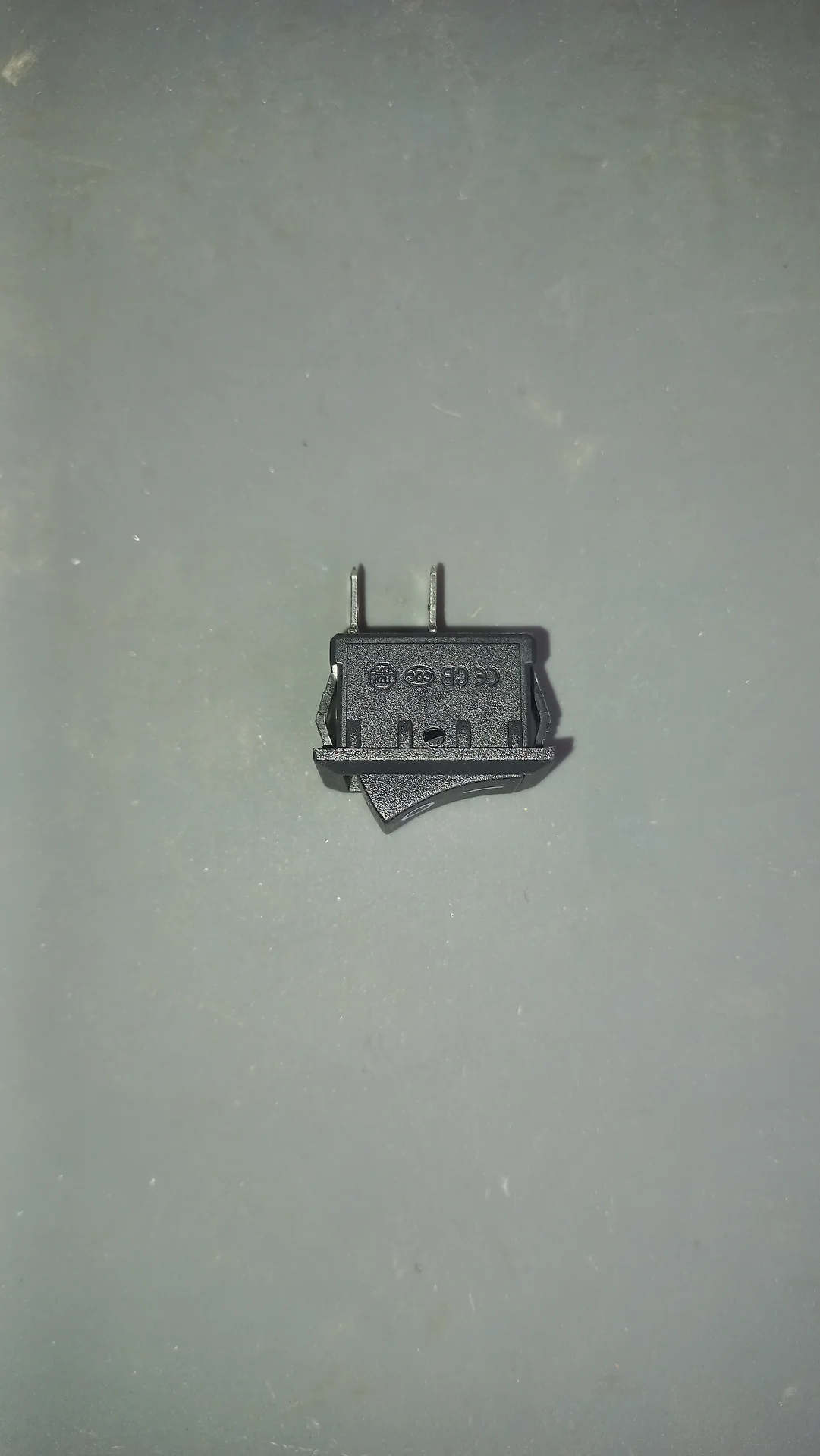 The same mini rocker switch from the back showing the CE and CCC certification marks and the two wiring pins