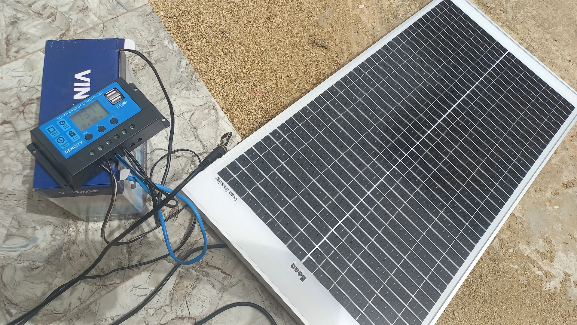 Wider shot of the same outdoor power-system test showing the panel, battery and controller wired up on the ground
