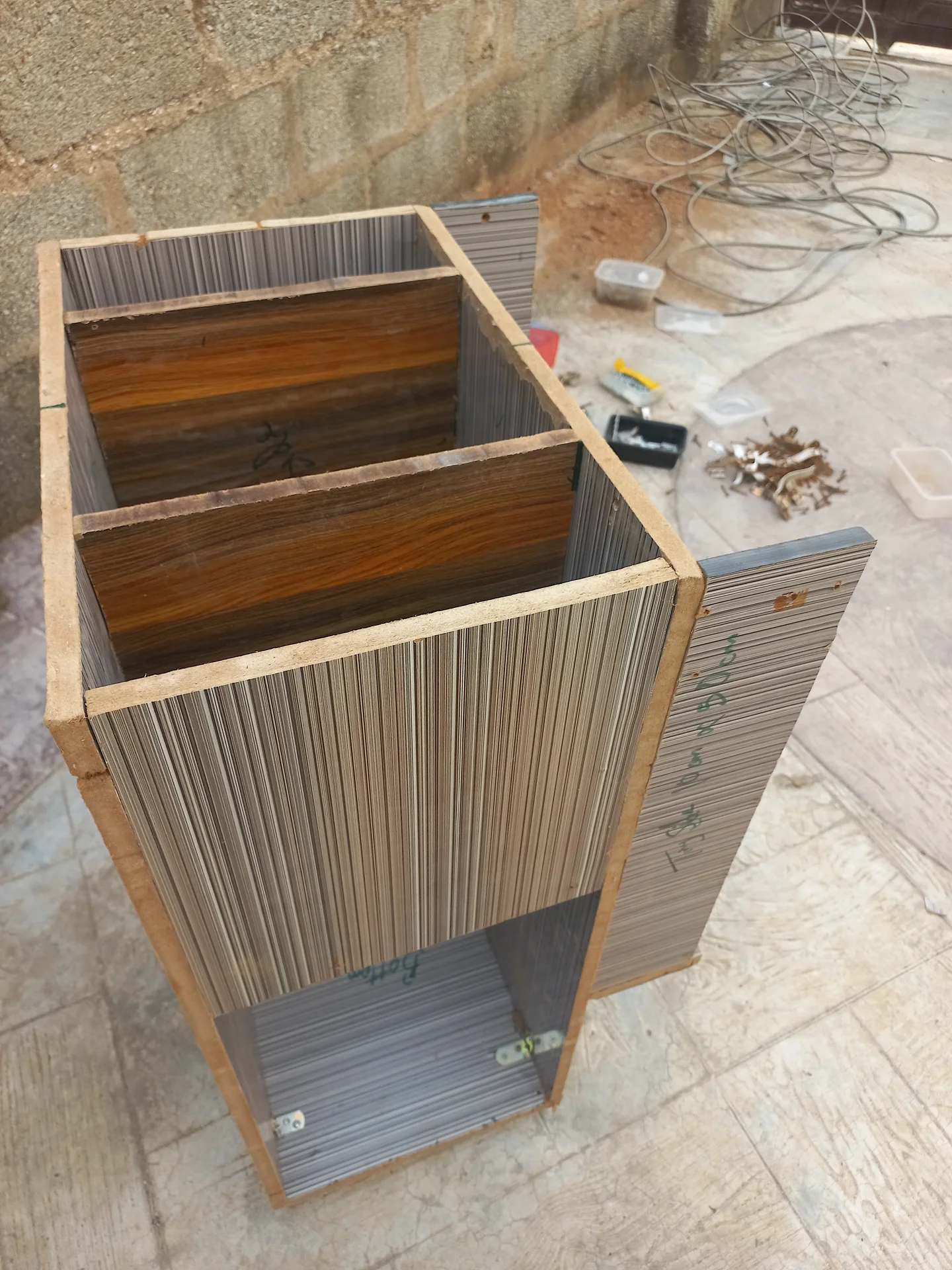 Angled front view of the bin showing the two upper sorting compartments with plywood floors and the lower open bay, with the right side panel partially open