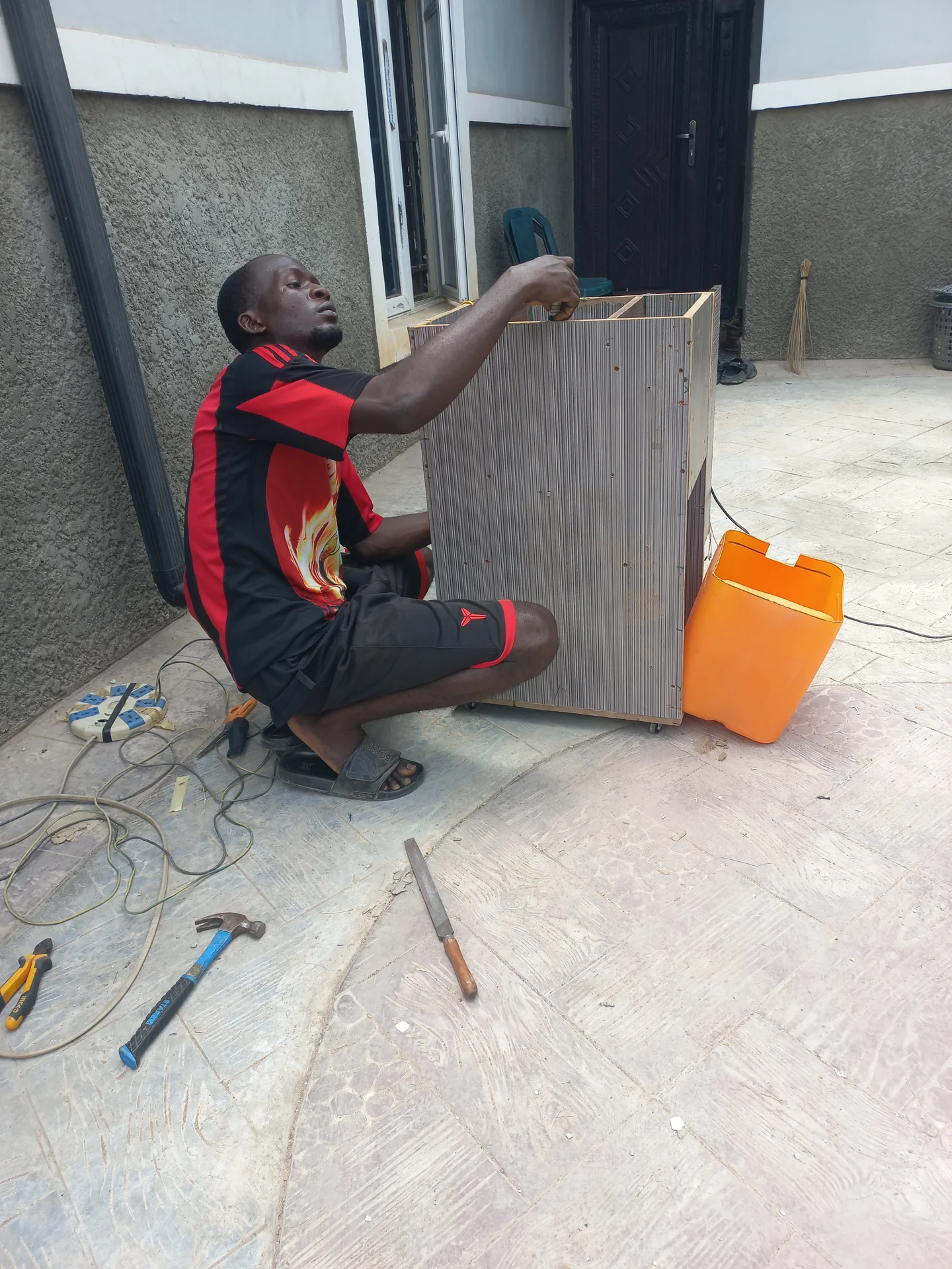 Builder crouching and reaching into the open top of the upright bin enclosure to fit internal components