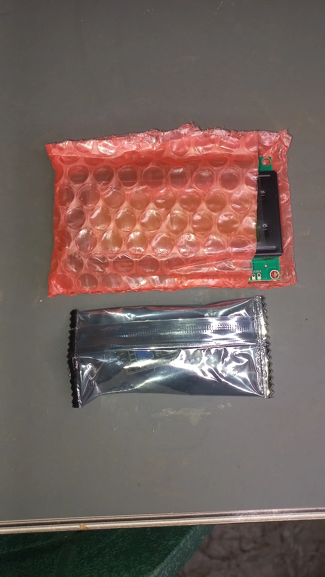 Two electronic modules in their delivery packaging: one in a red bubble-wrap protective pouch and one in a silver anti-static bag
