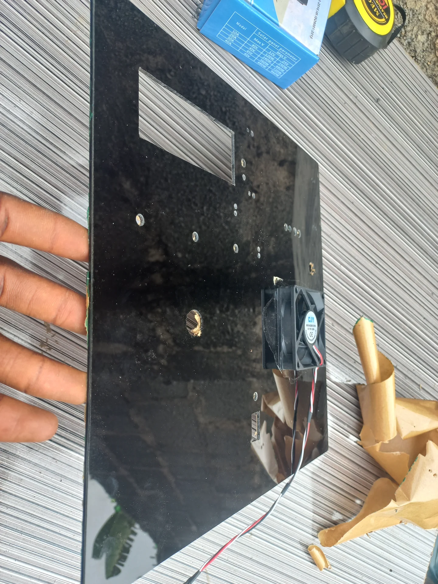 The black acrylic panel with the cooling fan mounted and standoffs fitted, showing the hole layout with some components already installed
