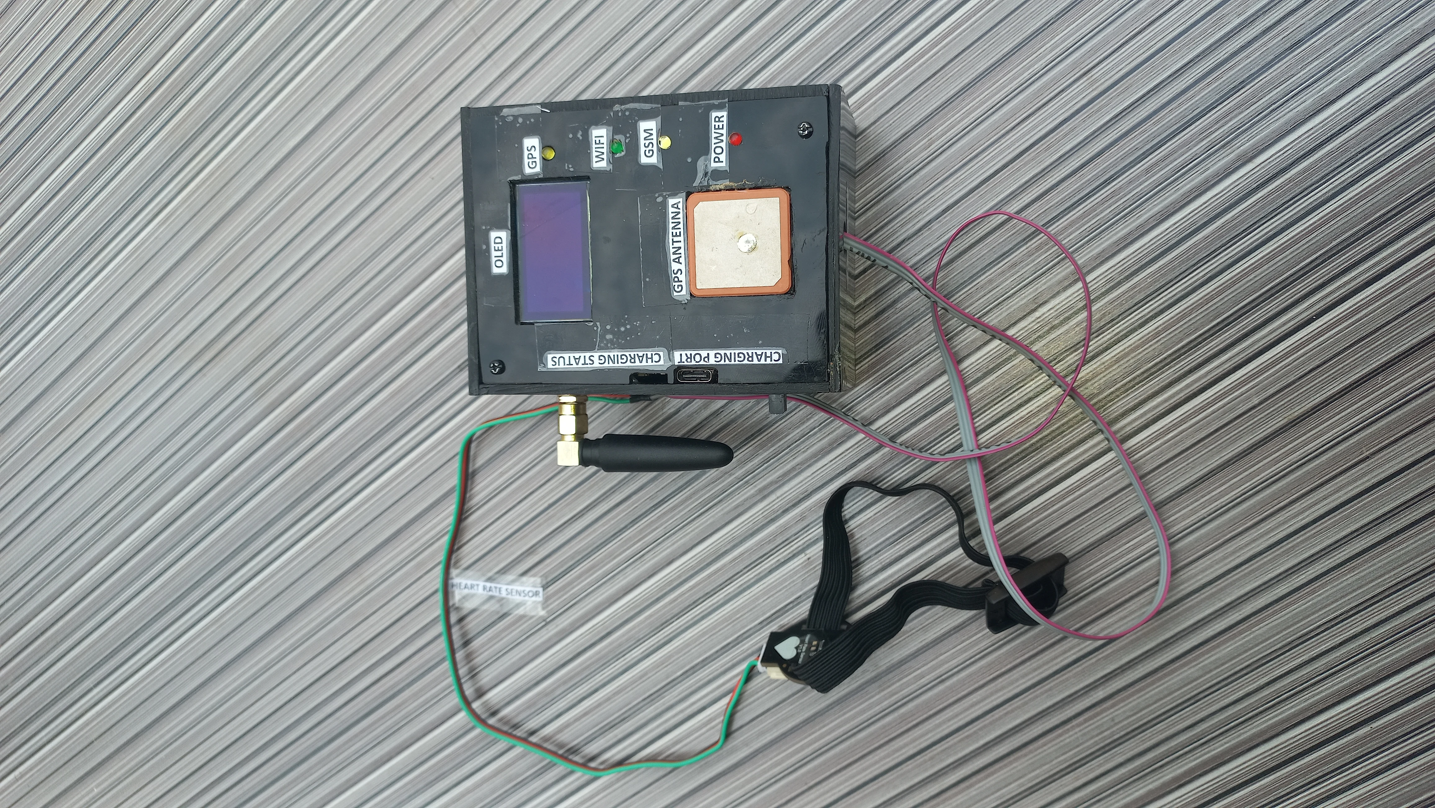Complete IoT Safety Device - overhead flat-lay showing enclosure with OLED, GPS patch antenna, PPG clip sensor, and labelled ports