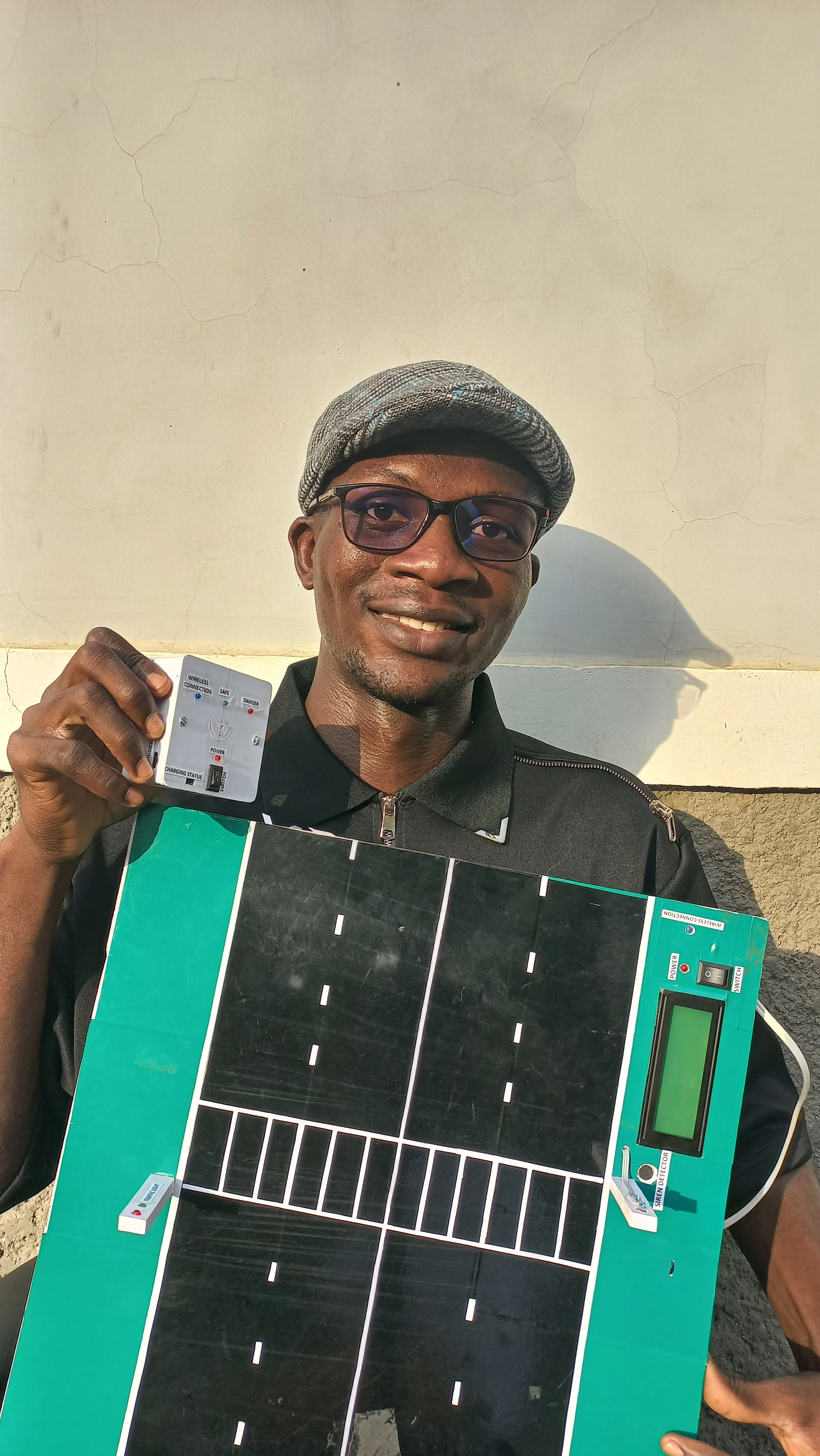 Developer smiling while holding both completed units: wearable unit in right hand, road model in left hand
