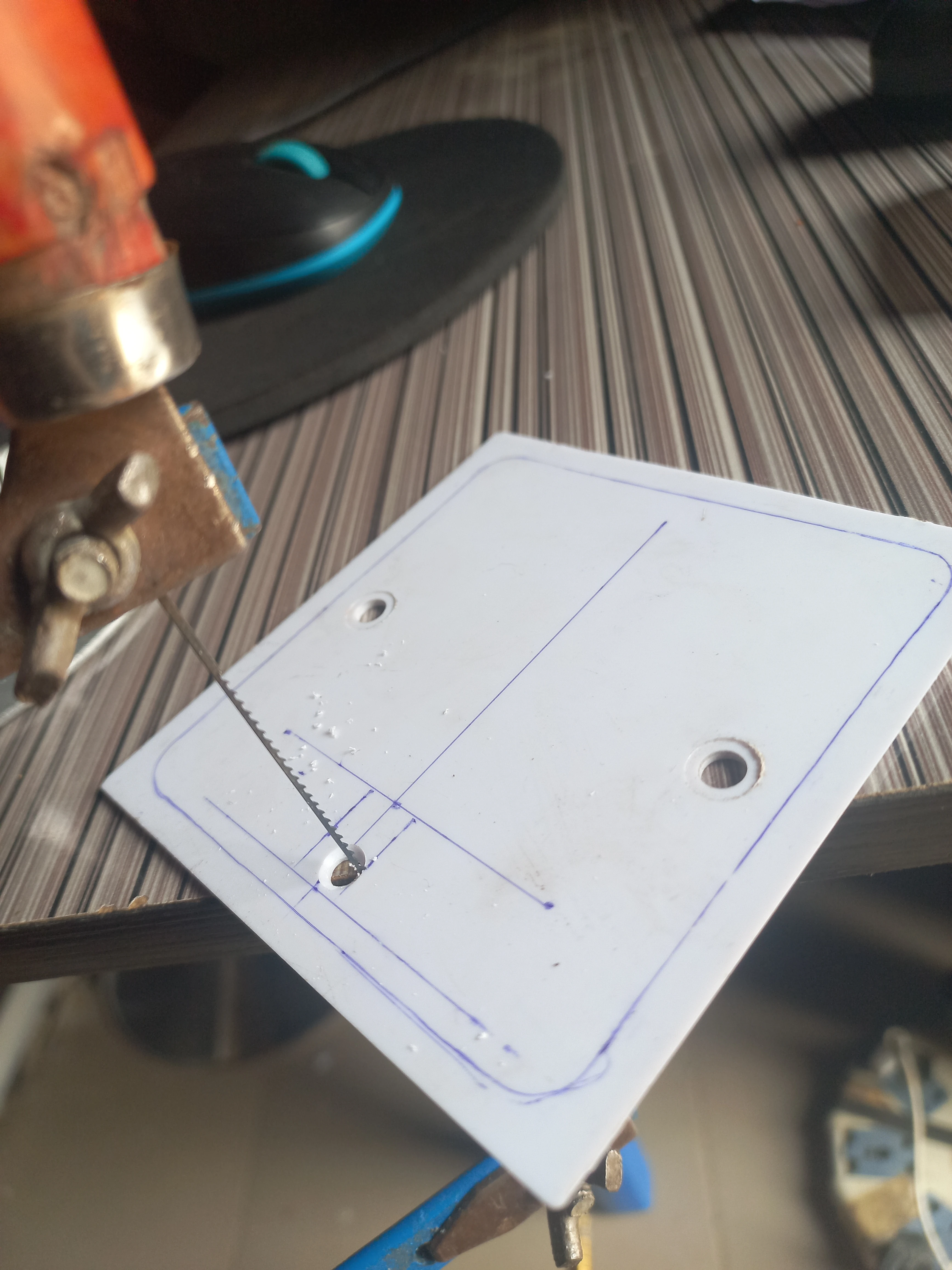 Hacksaw cutting through the PVC enclosure panel to create a component aperture