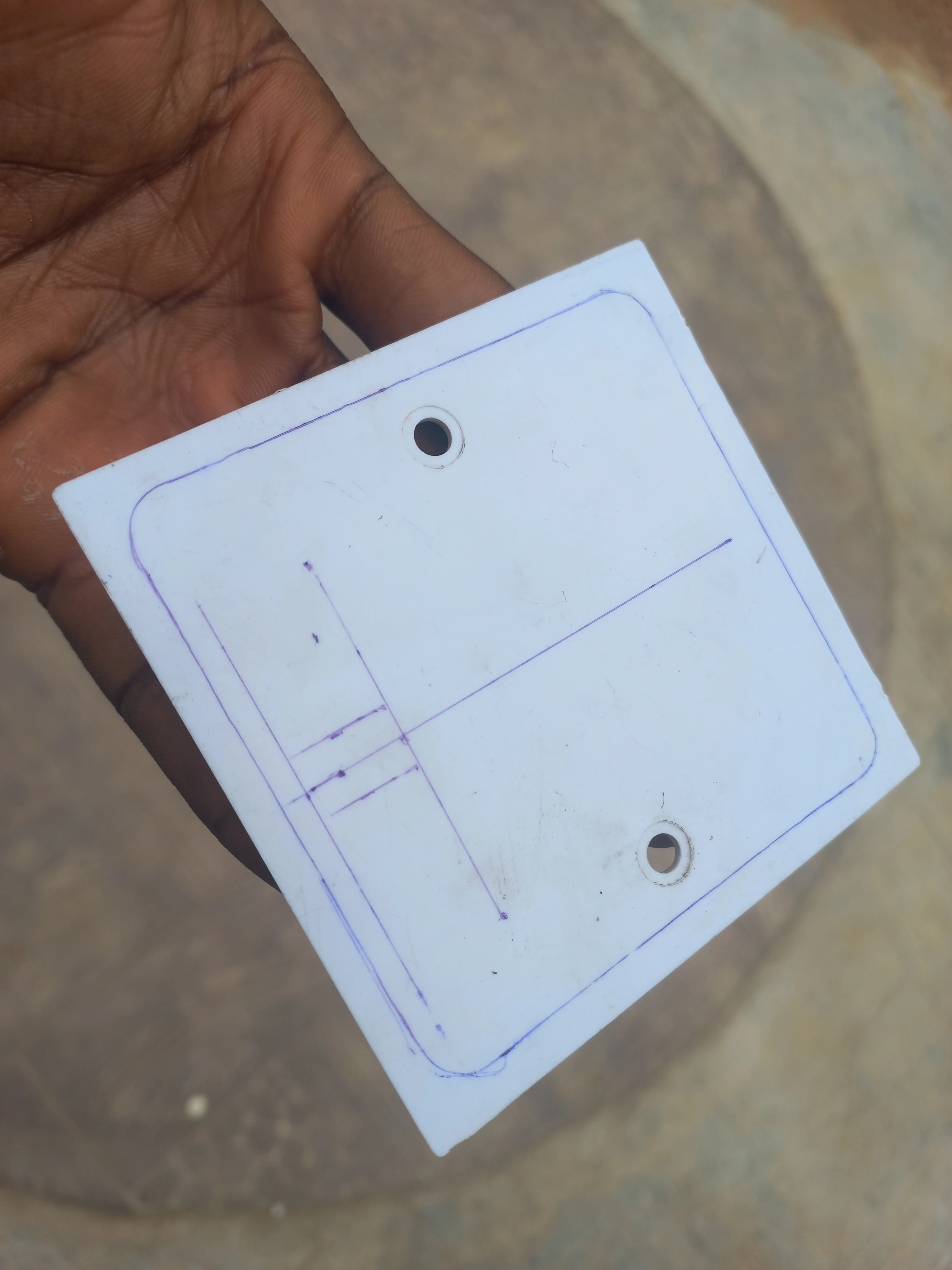 White PVC junction box cover plate with component cutout positions marked in pencil before cutting
